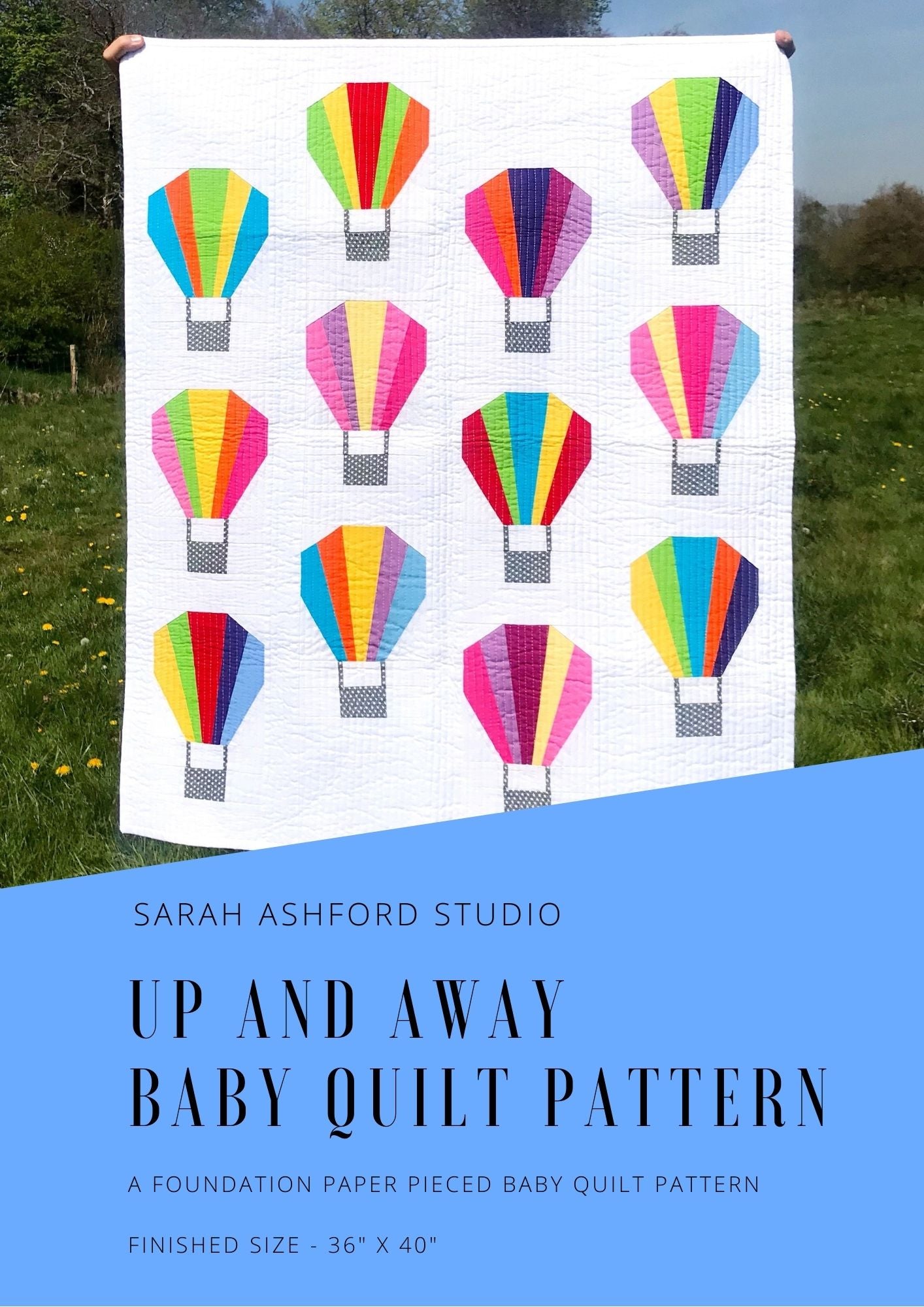 A baby quilt pattern. A baby quilt has a series of 12 hot air balloons, each made up of solid strips of colour against a backdrop of white.