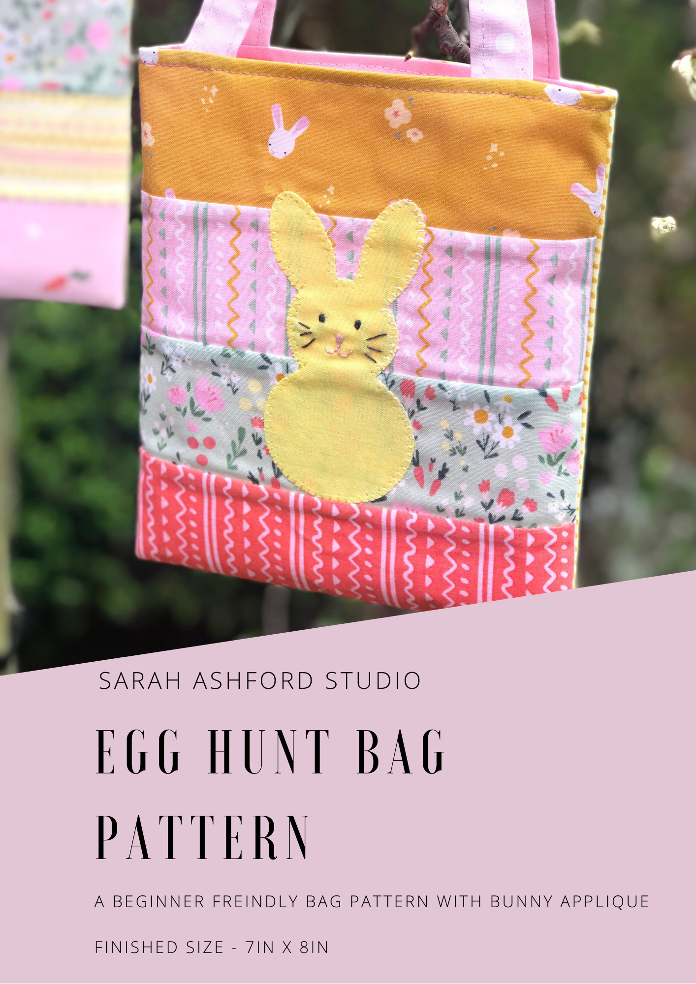 The egg hunt bag hangs from a tree. It has an applique rabbit in the centre, who has a cute face, pink nose and whiskers. The bag is made up of strips of summer themed fabric.